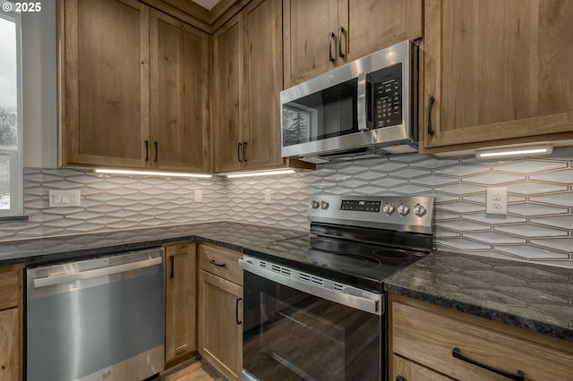 kitchen featuring dark stone counters, appliances with stainless steel finishes, brown cabinets, and tasteful backsplash