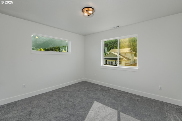 unfurnished room with baseboards, dark colored carpet, and visible vents