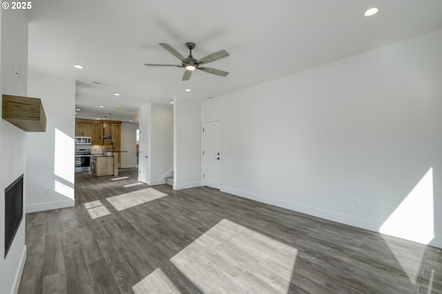 unfurnished living room with a ceiling fan, recessed lighting, stairs, and dark wood-type flooring