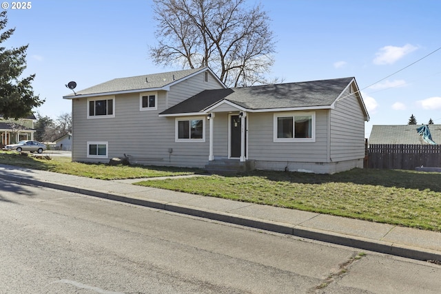 split level home with roof with shingles, a front yard, and fence