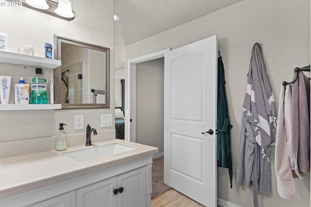 full bathroom featuring vanity, wood finished floors, a textured wall, and a shower