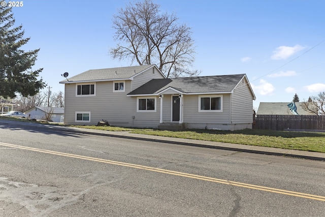 split level home with a shingled roof, a front yard, and fence