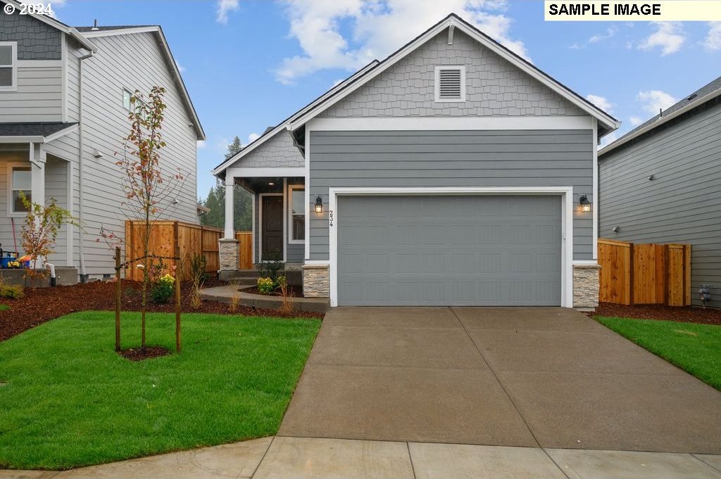 view of front facade featuring concrete driveway, fence, stone siding, and a front lawn