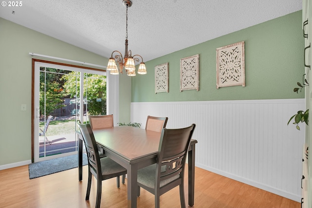 4420 NW 187th Ave, Portland, OR 97229 - dining space featuring light wood-style floors, a chandelier, a textured ceiling, a wainscoted wall, and vaulted ceiling