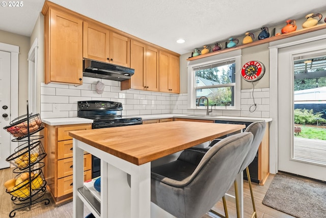 kitchen featuring butcher block countertops, sink, a breakfast bar, backsplash, and electric range