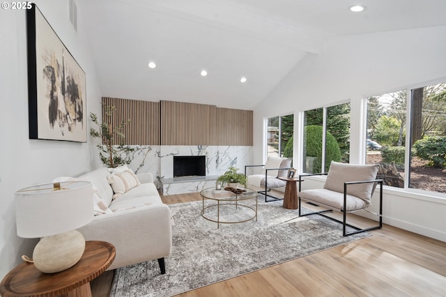 living room featuring high vaulted ceiling, a high end fireplace, light hardwood / wood-style floors, and beamed ceiling