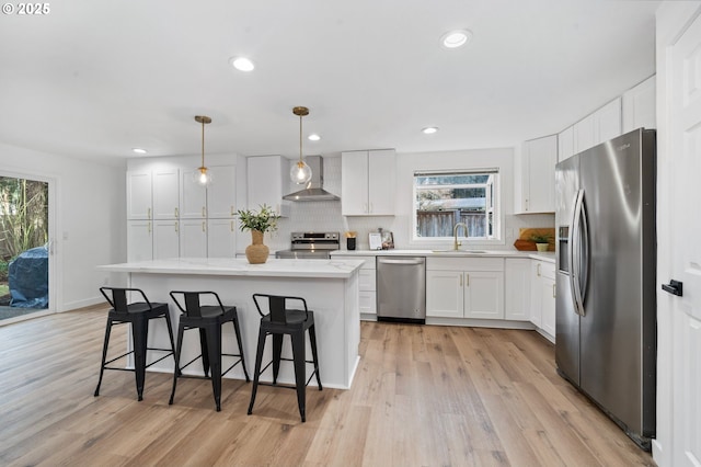 kitchen featuring wall chimney exhaust hood, white cabinetry, hanging light fixtures, appliances with stainless steel finishes, and a kitchen island