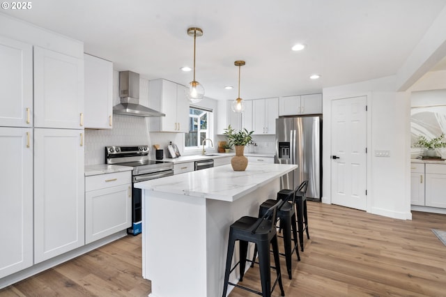 kitchen featuring white cabinetry, light stone counters, a center island, appliances with stainless steel finishes, and wall chimney range hood