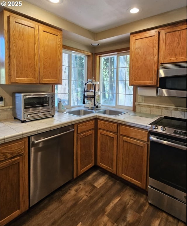 kitchen with appliances with stainless steel finishes, a sink, dark wood-style floors, tile countertops, and recessed lighting