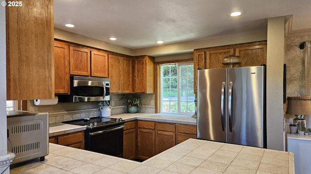 kitchen with stainless steel appliances, tile counters, heating unit, brown cabinets, and recessed lighting