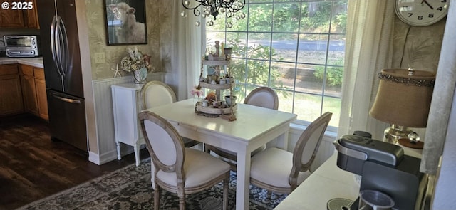 dining room featuring dark wood finished floors, a chandelier, wallpapered walls, a wainscoted wall, and healthy amount of natural light