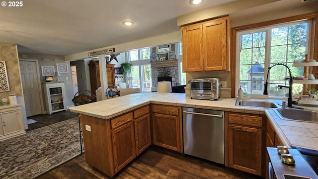 kitchen featuring stainless steel dishwasher, tile countertops, a stone fireplace, a peninsula, and recessed lighting