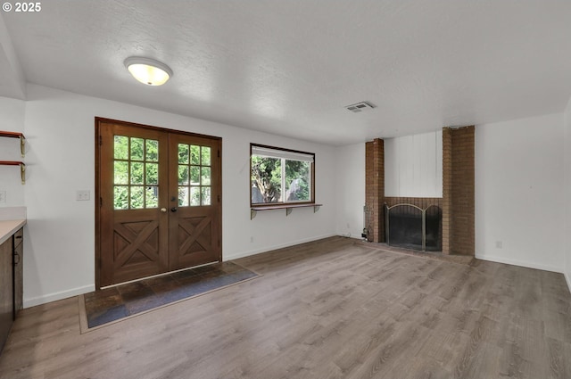 unfurnished living room with wood finished floors, french doors, a fireplace, baseboards, and a textured ceiling