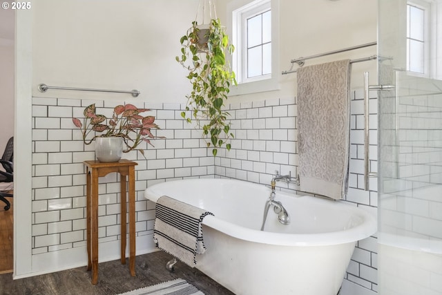 bathroom featuring plenty of natural light, a freestanding bath, and tile walls