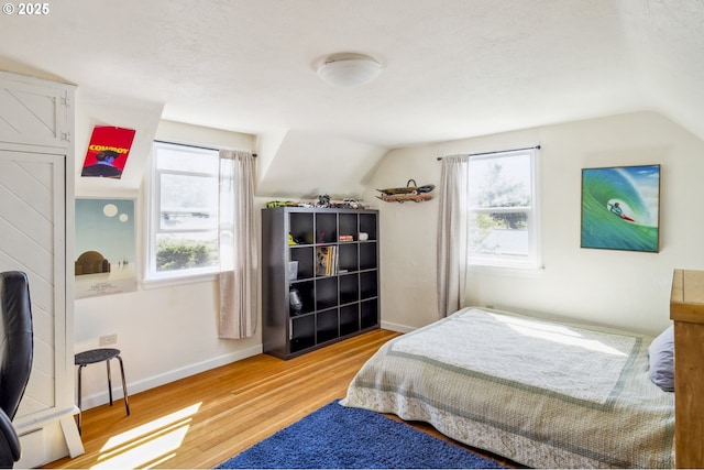 bedroom featuring vaulted ceiling, wood finished floors, multiple windows, and baseboards