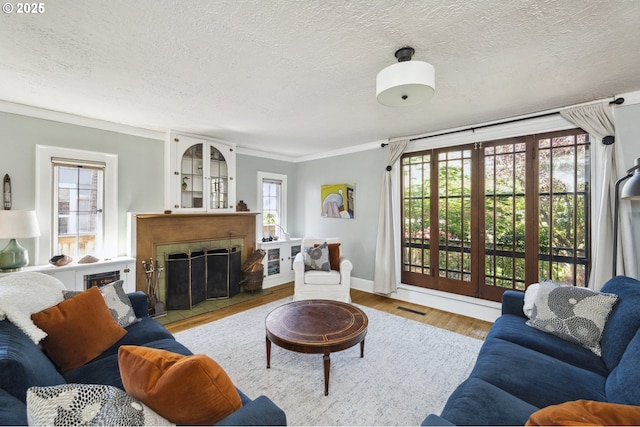 living area featuring a textured ceiling, ornamental molding, a fireplace with flush hearth, wood finished floors, and plenty of natural light