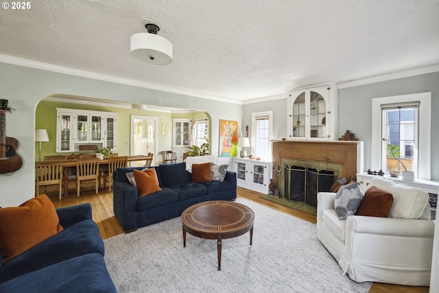 living area featuring arched walkways, wood finished floors, ornamental molding, a textured ceiling, and healthy amount of natural light