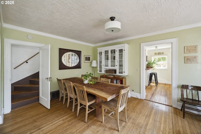 dining room featuring light wood-type flooring, crown molding, stairs, baseboards, and a textured ceiling