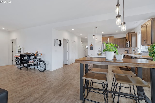 kitchen featuring light wood finished floors, stainless steel microwave, a breakfast bar, decorative light fixtures, and backsplash