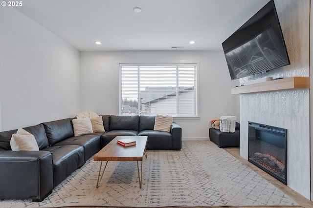 living room featuring a glass covered fireplace, visible vents, baseboards, and recessed lighting