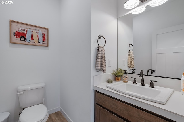 half bath featuring toilet, baseboards, wood finished floors, and vanity