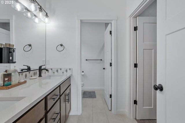 bathroom featuring tile patterned flooring, toilet, a sink, baseboards, and double vanity