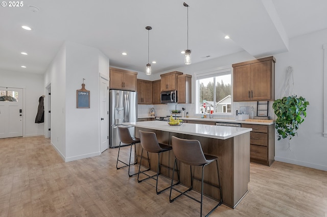 kitchen featuring a breakfast bar area, light wood-style flooring, stainless steel appliances, a kitchen island, and tasteful backsplash