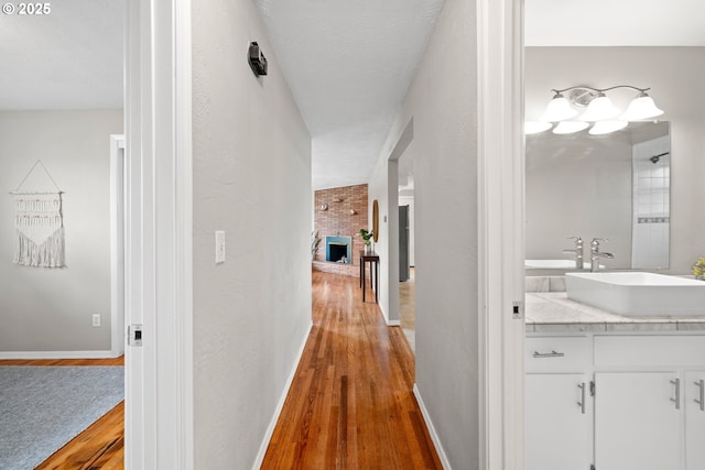 corridor featuring a textured wall, wood finished floors, baseboards, and a sink