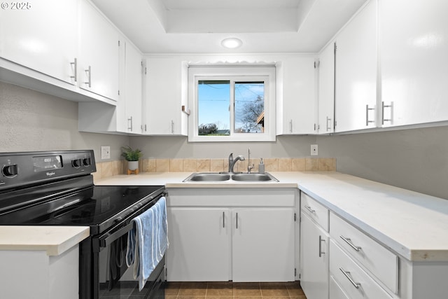 kitchen with black electric range, a raised ceiling, white cabinetry, and a sink