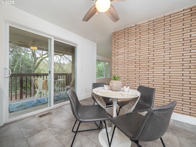 dining space featuring visible vents, baseboards, ceiling fan, and brick wall