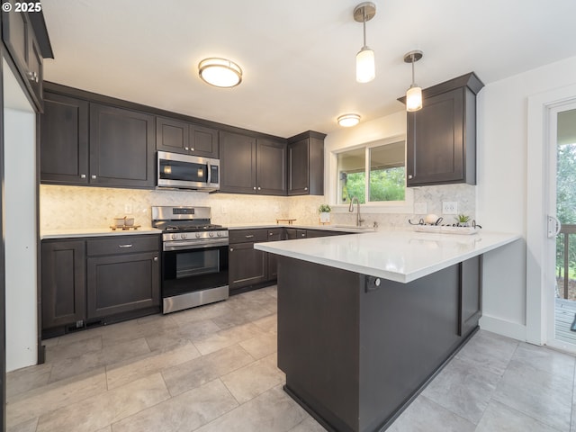 kitchen with backsplash, light countertops, appliances with stainless steel finishes, a peninsula, and a sink