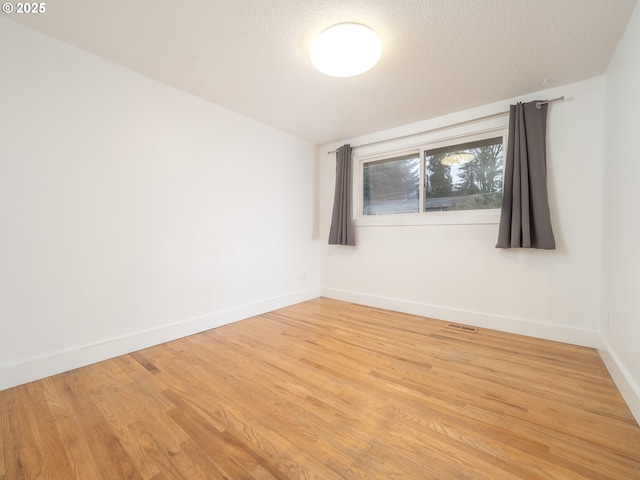 unfurnished room with visible vents, light wood-style floors, baseboards, and a textured ceiling