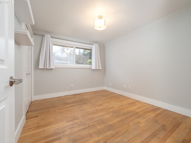 empty room with baseboards, light wood finished floors, and a textured ceiling