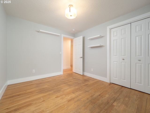 unfurnished bedroom featuring light wood-style flooring, baseboards, a closet, and a textured ceiling