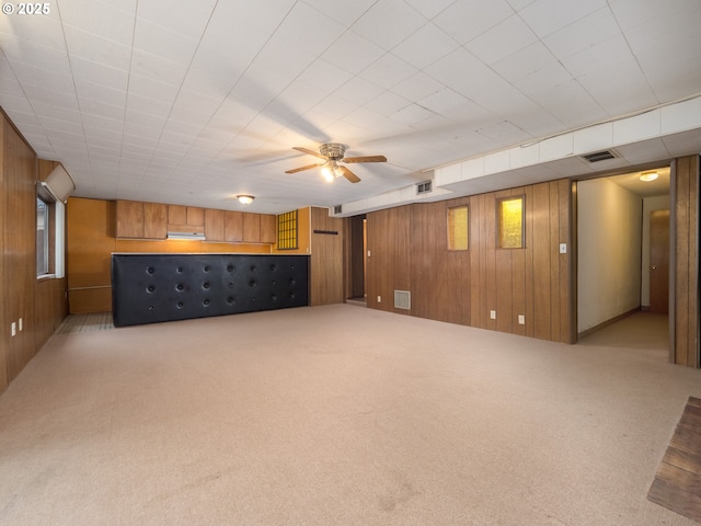 interior space featuring ceiling fan, visible vents, carpet floors, and wood walls