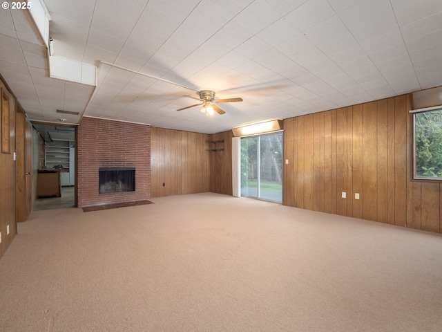 unfurnished living room with wooden walls, carpet flooring, a brick fireplace, and ceiling fan