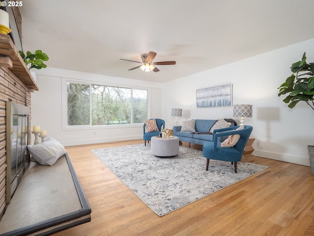 living area featuring a ceiling fan, a brick fireplace, wood finished floors, and baseboards