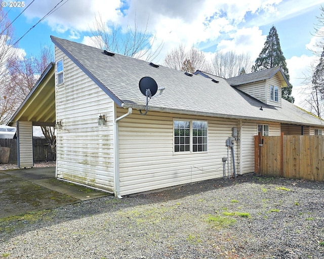 view of side of home with a carport, a shingled roof, gravel driveway, and fence