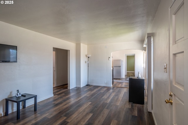 living room with arched walkways, dark wood finished floors, and baseboards