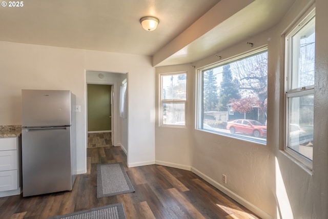 kitchen with dark wood-style floors, light stone counters, freestanding refrigerator, and baseboards