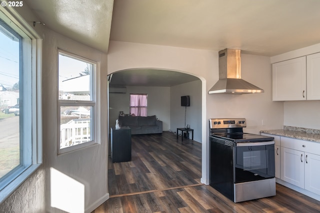 kitchen with arched walkways, wall chimney range hood, white cabinets, and stainless steel range with electric cooktop