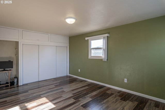 unfurnished bedroom with a closet, baseboards, and dark wood-style flooring