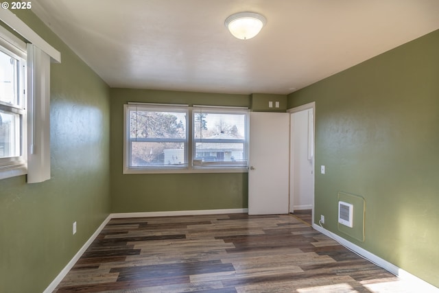 empty room with dark wood-type flooring, visible vents, and baseboards