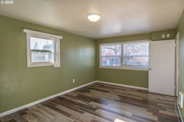 spare room featuring dark wood-type flooring, plenty of natural light, and baseboards