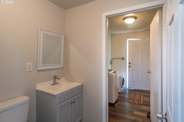 half bathroom featuring toilet, vanity, washing machine and clothes dryer, and wood finished floors