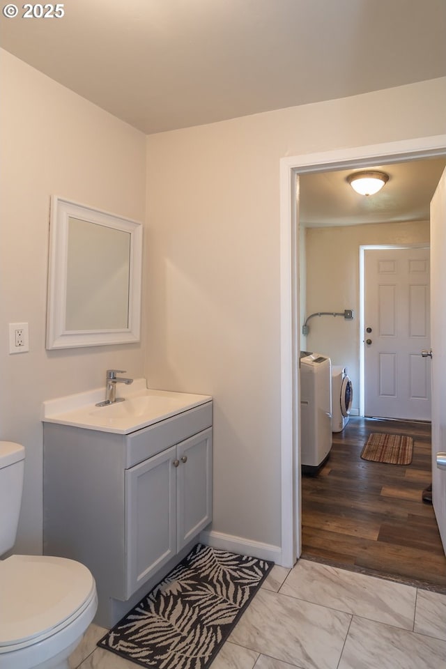 half bath with marble finish floor, toilet, vanity, separate washer and dryer, and baseboards