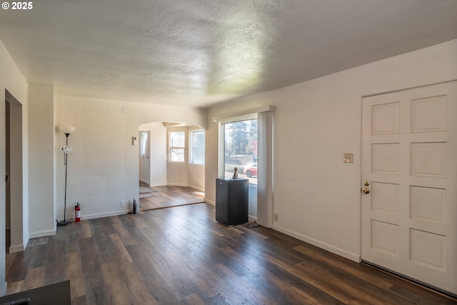 unfurnished living room with dark wood-style floors, arched walkways, a textured ceiling, and baseboards