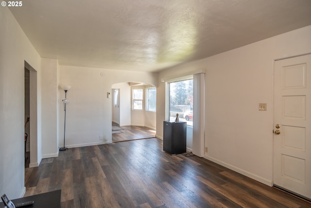 unfurnished living room featuring dark wood-style floors, arched walkways, and baseboards