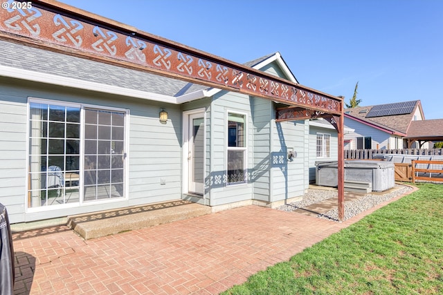 exterior space featuring a patio area, a hot tub, fence, and a shingled roof