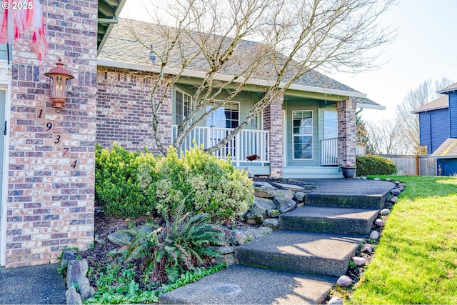 property entrance with covered porch, brick siding, and roof with shingles